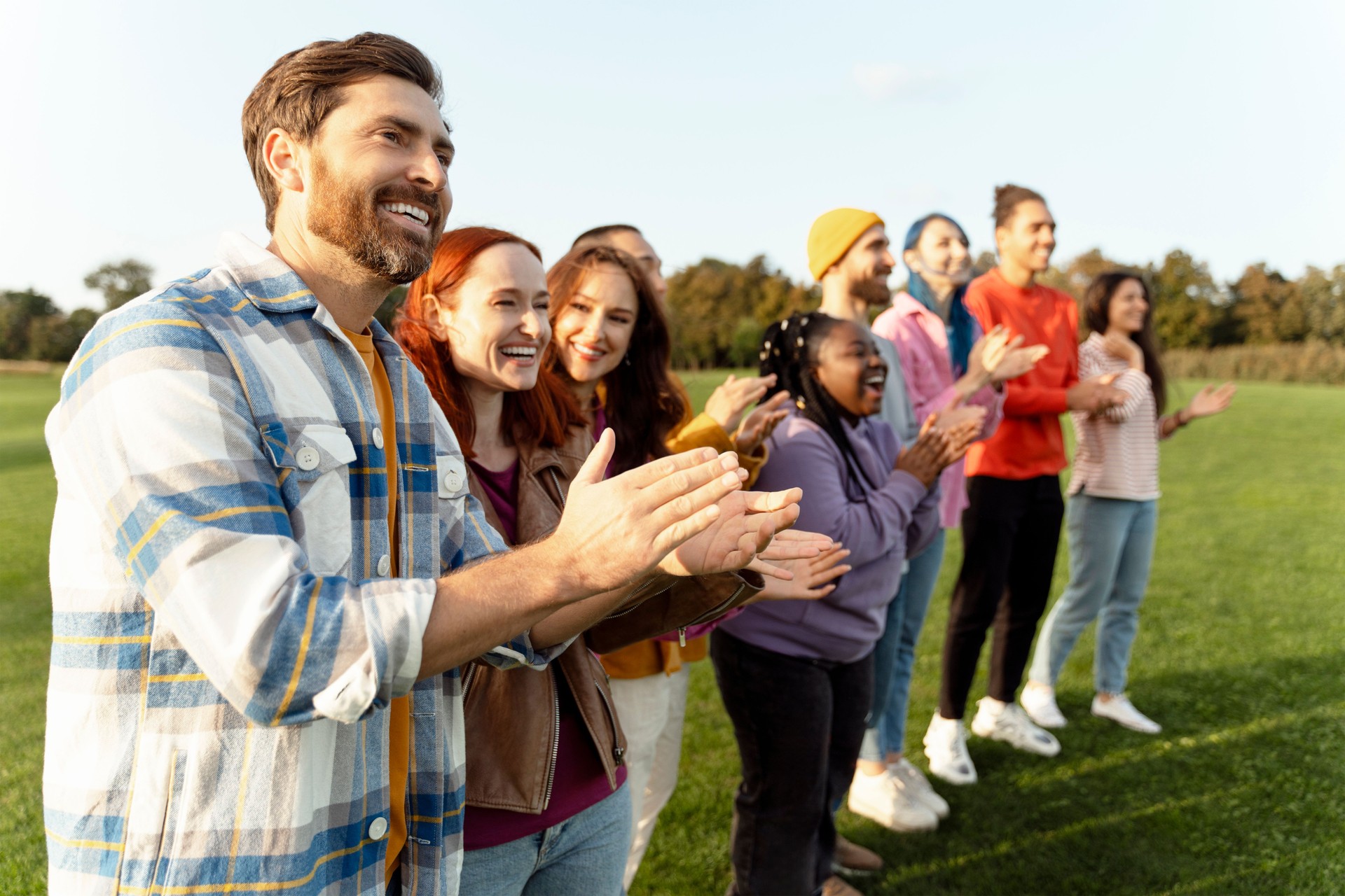 Happy and diverse group of people clapping hands together outdoors